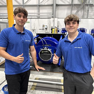 2 junge Männer stehen vor einem ZIEHL-ABEGG-Produkt & zeigen Daumen nach oben
